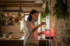 Middle Eastern woman pouring fragrance oil into red mosaic wall plug-in warmer plugged into kitchen wall - French country kitchen